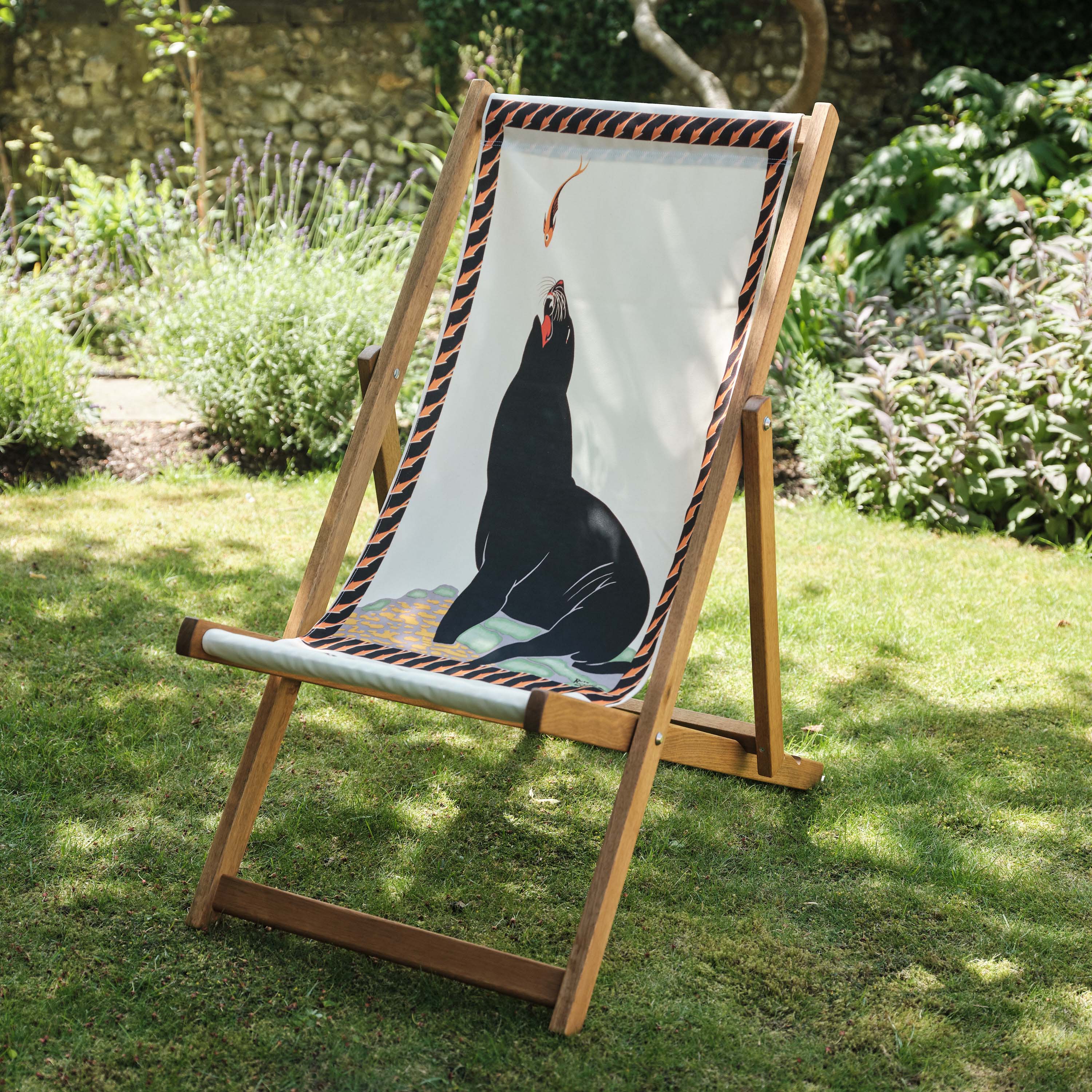 Wooden deck chairs with illustrated fabric seat, set on a garden lawn for outdoor relaxation