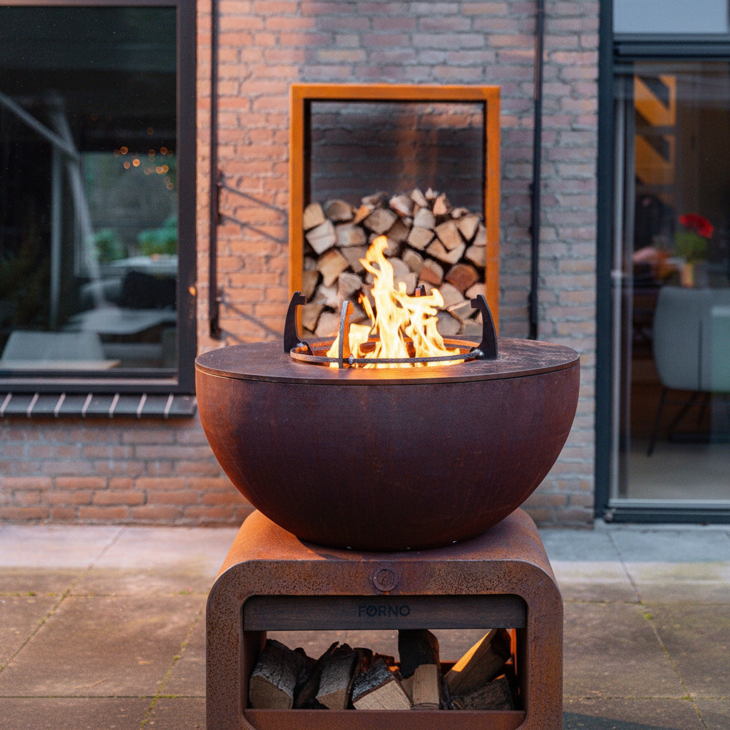 Close up of Corten Steel Seare Bole Plancha Grill with log store behind