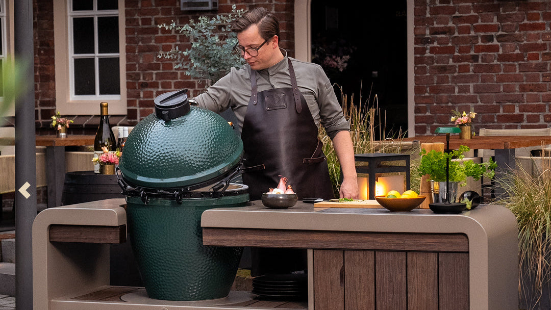Person preparing food outdoors with a large Kamado cooking station with big green egg grill on a wooden table.