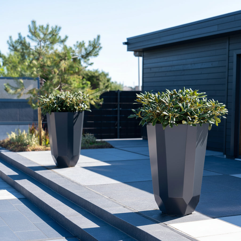 Two modern grey aluminium facet planters with green plants on a patio