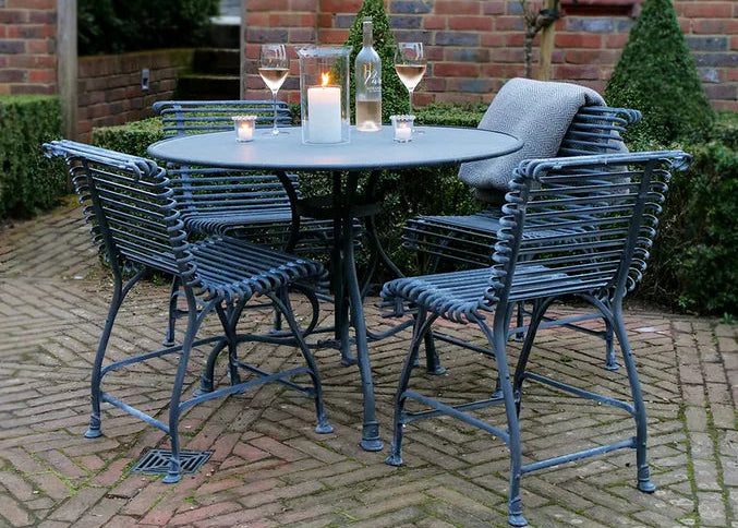 Outdoor galvanised zinc Arras dining set set with table, chairs, candles, and wine glasses on a brick patio.