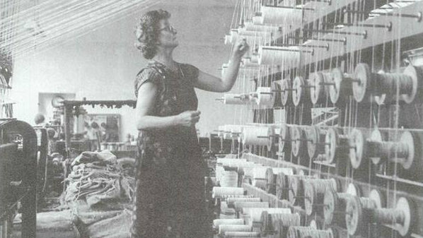 Woman standing in a textile mill surrounded by spools of garden twine