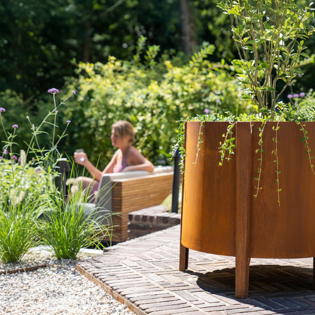 Person sitting on a bench in a garden with a large Adezz Corten steel Botan planter in the foreground.
